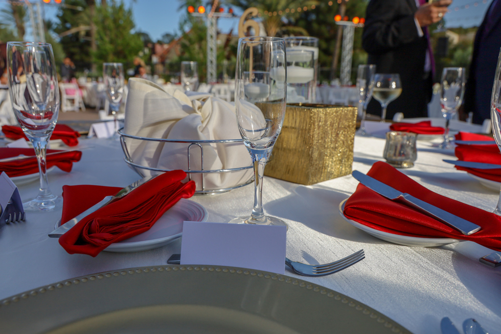 Elegant outdoor event table setup with glasses, red napkins, and gold decorations. Perfect for weddings and formal gatherings in Wilmington, DE.