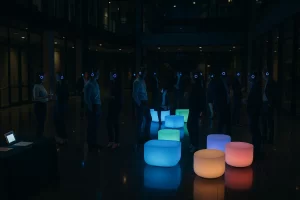 Corporate atrium after hours with coworkers dancing in headphones, LED lounge furniture, and a tidy check‑in station.