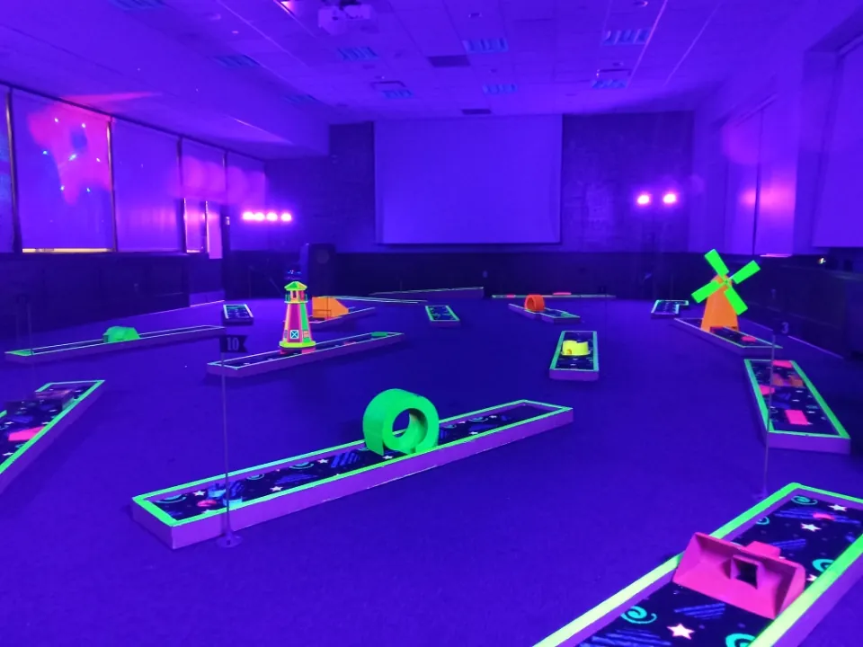 Black-light mini golf course with glowing holes, a windmill and a lighthouse set up indoors