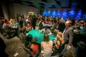 Casino night with dealers running blackjack tables for a crowd of guests in a dark event hall