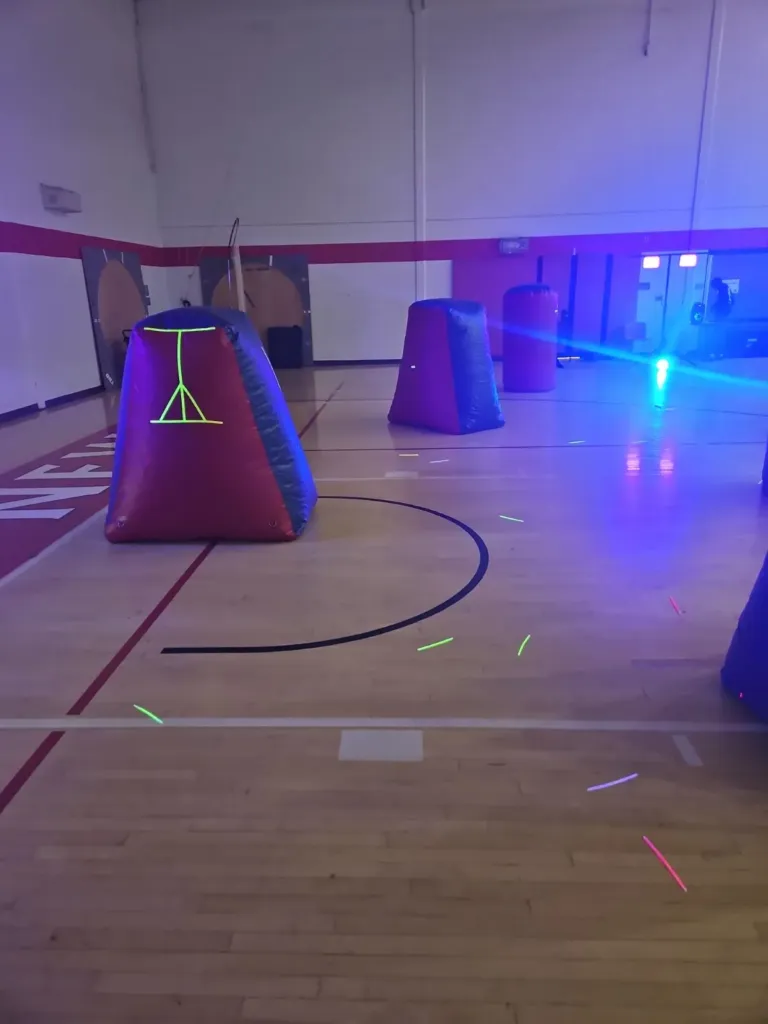 Open-air laser tag bunkers set up across a school gym floor under blue and black lighting