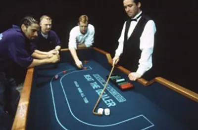 Dealer in a vest running a Beat the Dealer dice table while guests watch the roll
