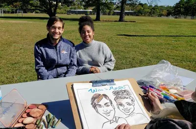 Caricature artist showing a finished drawing to two guests at an event table