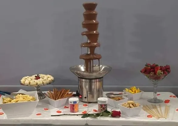 Chocolate fountain on a dessert table surrounded by fruit and treats for dipping