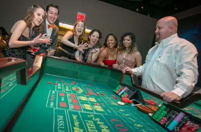 Craps dealer running a full-size craps table as smiling guests cheer from the rail