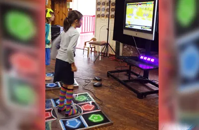Young girl stepping on the glowing arrow pads of a dance arcade game in front of a screen at an indoor party