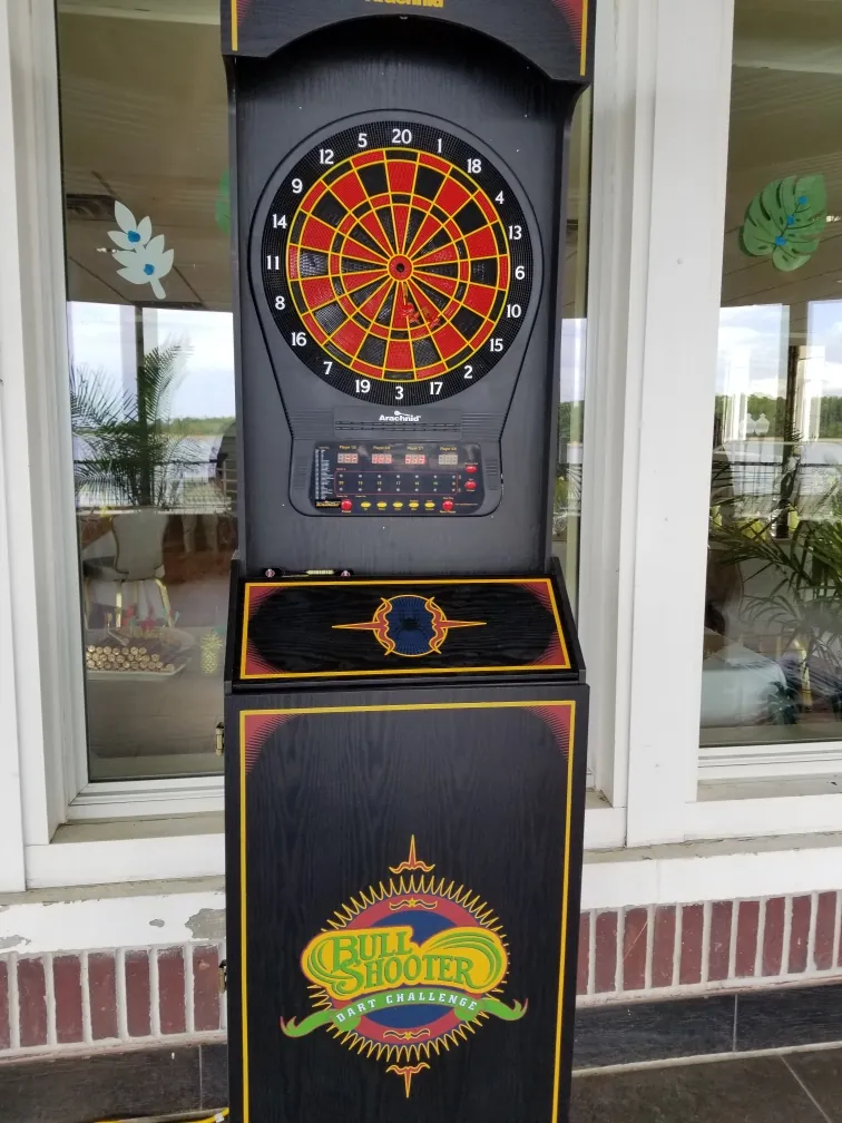 Electronic dartboard arcade cabinet with a lit scoring display standing by a window at an event venue