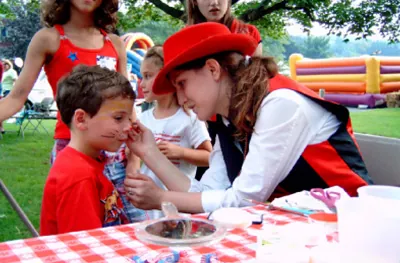 Face painter painting a young boy at an outdoor party table