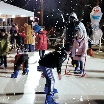 Kids and parents skating on a synthetic ice rink at an outdoor winter event