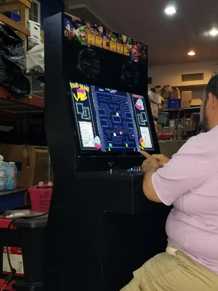 Guest playing a Multicade multi-game arcade cabinet with a two-player joystick and button panel and a classic maze game on screen