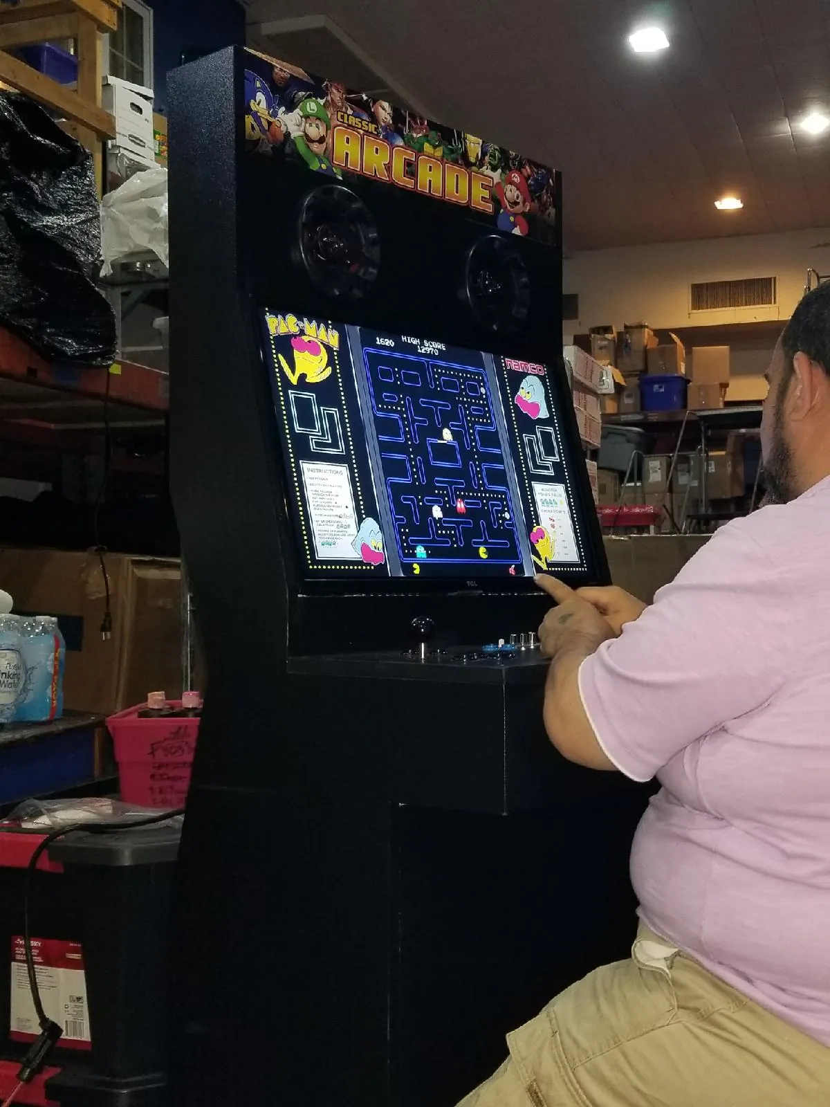 Guest playing a Multicade multi-game arcade cabinet with a two-player joystick and button panel and a classic maze game on screen
