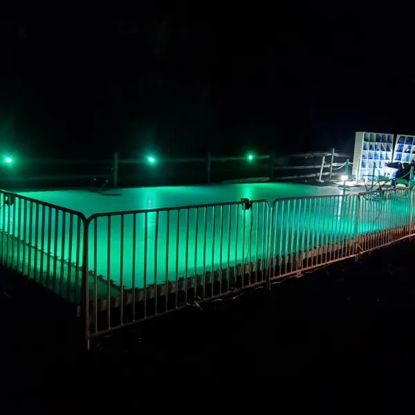 Portable synthetic ice rink lit green at night inside a ring of metal barricades