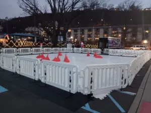 Synthetic ice rink with white dasher boards and skate cones set up on a paved parking lot