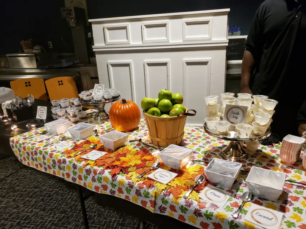 Caramel apple dipping station with green apples, toppings and a pumpkin on a festive table
